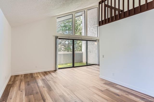 unfurnished room with baseboards, a textured ceiling, high vaulted ceiling, and wood finished floors