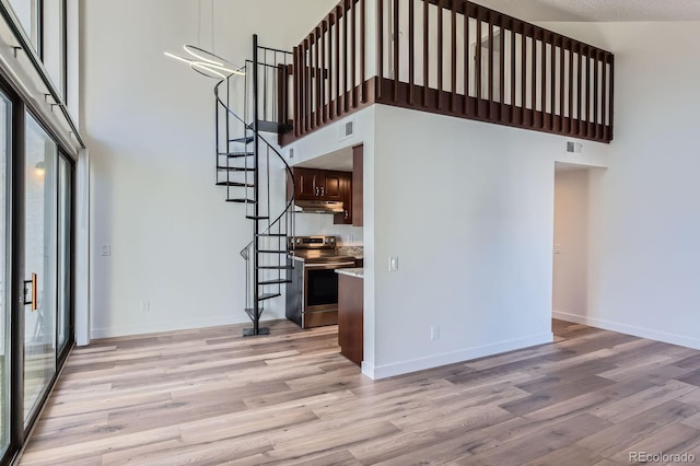 unfurnished living room featuring baseboards, a towering ceiling, and light wood finished floors