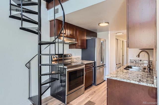 kitchen featuring light wood-style flooring, light stone counters, stainless steel appliances, under cabinet range hood, and a sink