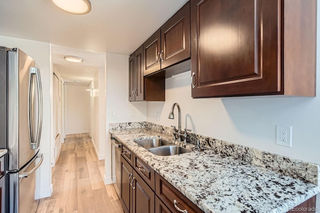 kitchen with dark brown cabinetry, appliances with stainless steel finishes, light stone countertops, light wood-type flooring, and a sink