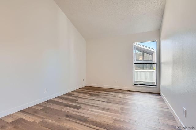 spare room with lofted ceiling, a textured ceiling, baseboards, and wood finished floors