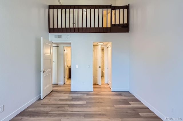 unfurnished bedroom with a towering ceiling, visible vents, baseboards, and wood finished floors