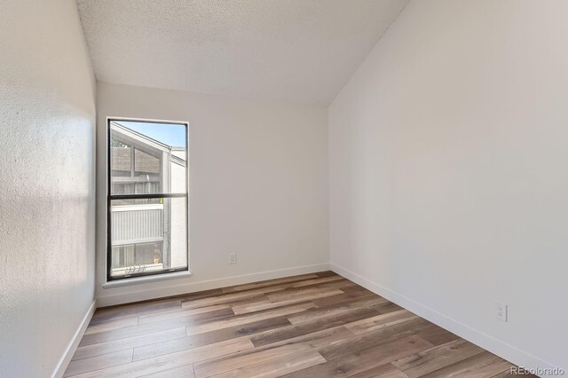 unfurnished room with a textured ceiling, wood finished floors, and baseboards