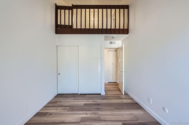 unfurnished bedroom featuring visible vents, a closet, baseboards, and wood finished floors