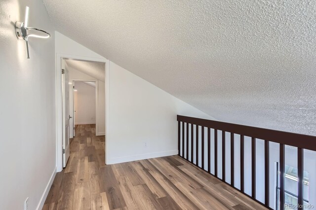 hall featuring a textured ceiling, vaulted ceiling, wood finished floors, and baseboards