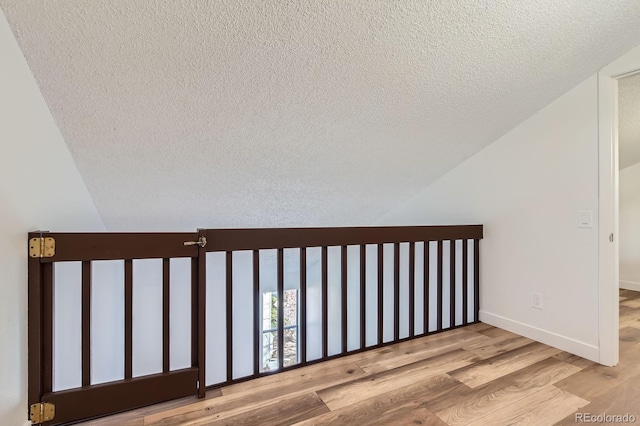 staircase with a textured ceiling, baseboards, vaulted ceiling, and wood finished floors