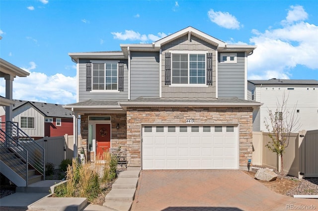 view of front of house featuring a garage, stone siding, driveway, and fence