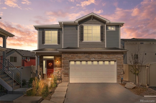 view of front of house featuring an attached garage, driveway, stone siding, and fence