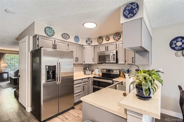 8252 S Fillmore Cir, Centennial, CO 80122 - kitchen featuring stainless steel appliances, gray cabinetry, light countertops, a textured ceiling, and light wood-type flooring