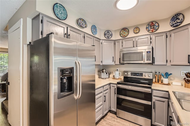 8252 S Fillmore Cir, Centennial, CO 80122 - kitchen with appliances with stainless steel finishes, gray cabinetry, light countertops, light wood-style flooring, and a textured ceiling