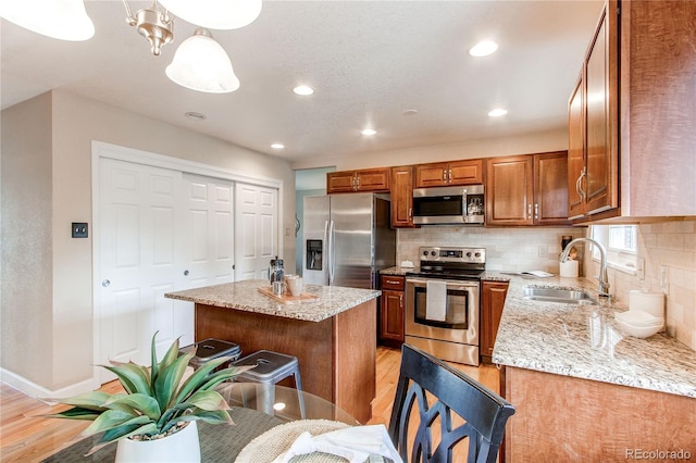 kitchen with light wood-style floors, a sink, brown cabinetry, and appliances with stainless steel finishes