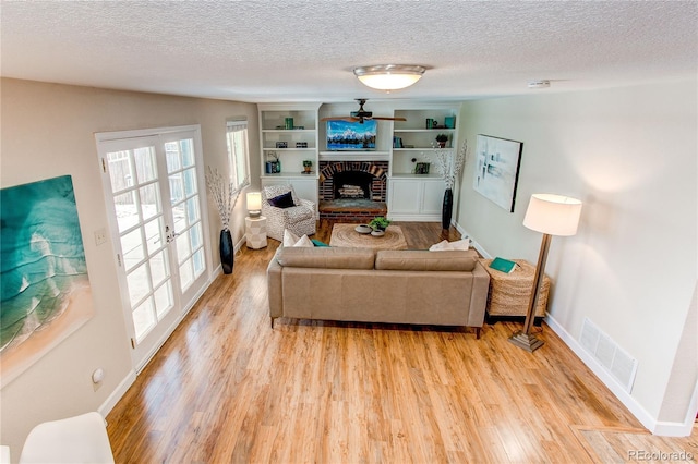 living area with a textured ceiling, visible vents, a brick fireplace, baseboards, and light wood-style floors