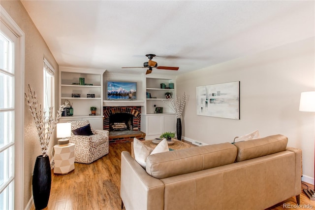 living area featuring a brick fireplace, a ceiling fan, baseboards, and wood finished floors
