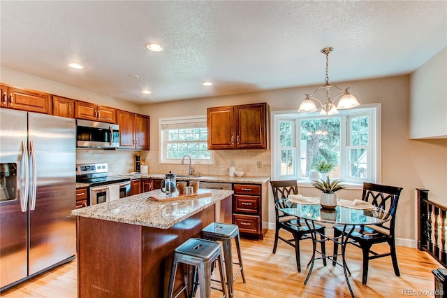 kitchen with light stone counters, light wood-style flooring, backsplash, and stainless steel appliances