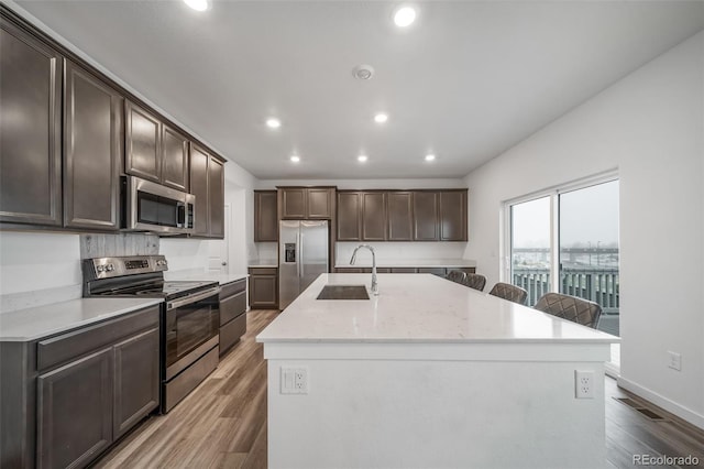 kitchen with an island with sink, light wood-type flooring, appliances with stainless steel finishes, and a sink