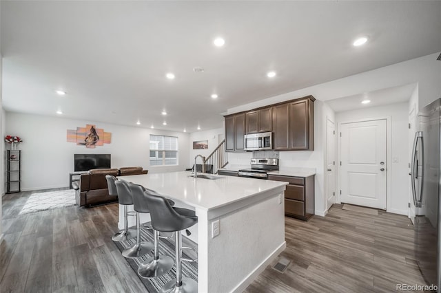 kitchen with a center island with sink, appliances with stainless steel finishes, dark wood-type flooring, a sink, and recessed lighting