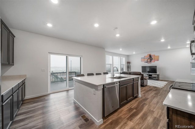 kitchen with a sink, dark wood-style flooring, stainless steel dishwasher, and an island with sink