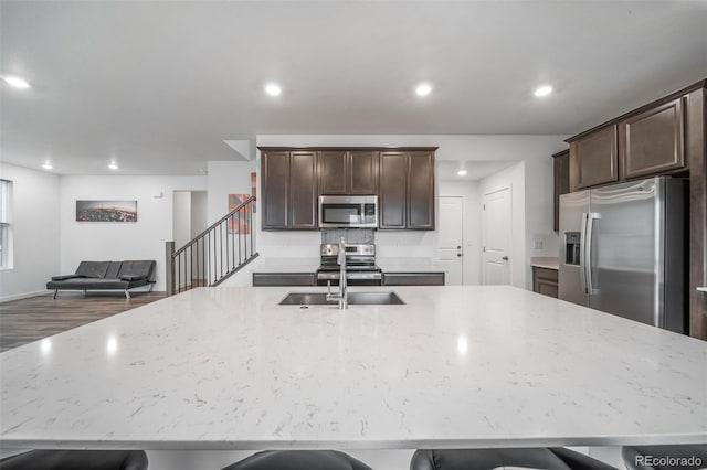 kitchen with light stone counters, stainless steel appliances, a sink, and a large island with sink