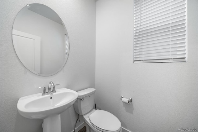 bathroom with toilet, a sink, and a textured wall