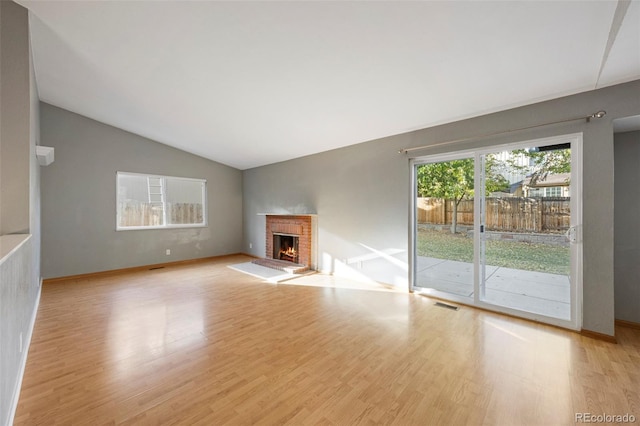 unfurnished living room featuring vaulted ceiling, light hardwood / wood-style flooring, and a brick fireplace