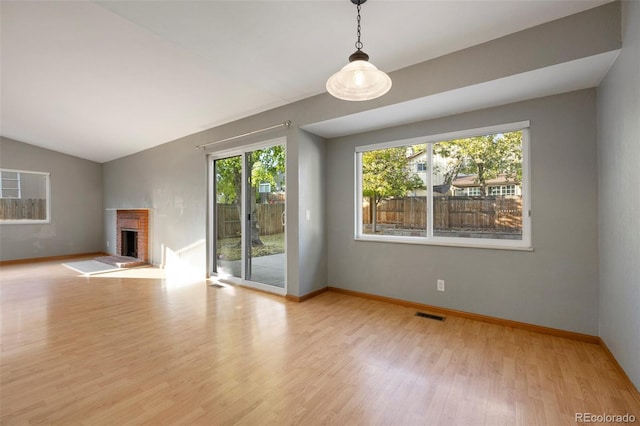 unfurnished living room featuring light hardwood / wood-style flooring, lofted ceiling, a wealth of natural light, and a brick fireplace