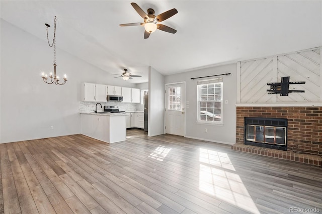 unfurnished living room with sink, a fireplace, vaulted ceiling, and light wood-type flooring