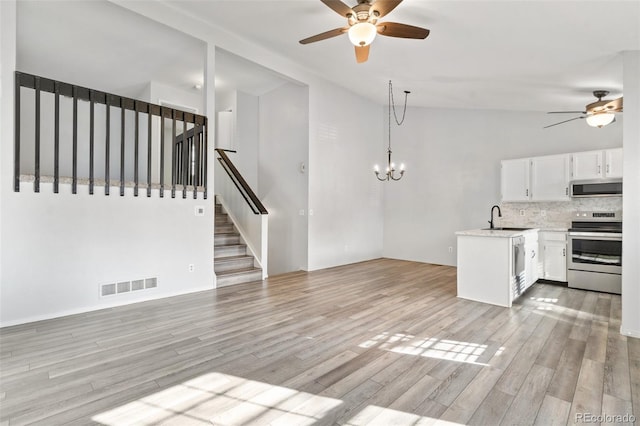 unfurnished living room with ceiling fan with notable chandelier, sink, vaulted ceiling, and light hardwood / wood-style flooring