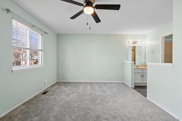 unfurnished bedroom featuring dark colored carpet, sink, ceiling fan, and ensuite bath