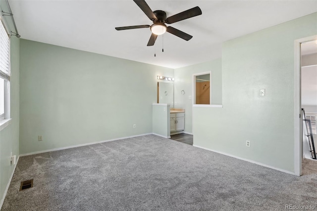 unfurnished bedroom with dark colored carpet, connected bathroom, and ceiling fan