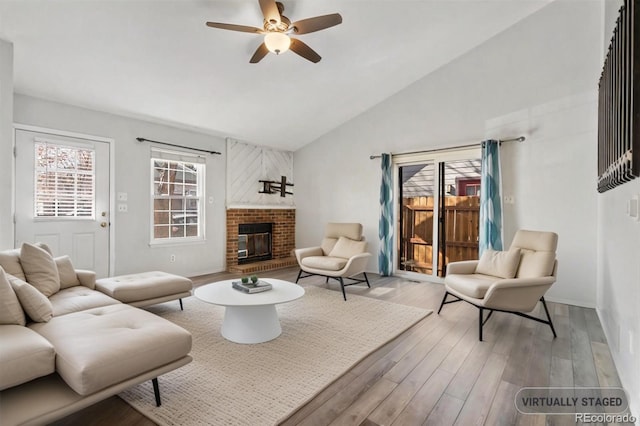 living area with a brick fireplace, a ceiling fan, high vaulted ceiling, and wood finished floors