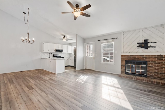 unfurnished living room featuring wood finished floors, lofted ceiling, a fireplace, a sink, and ceiling fan with notable chandelier