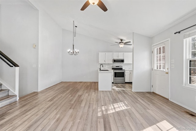 unfurnished living room with stairway, vaulted ceiling, ceiling fan with notable chandelier, and light wood-type flooring