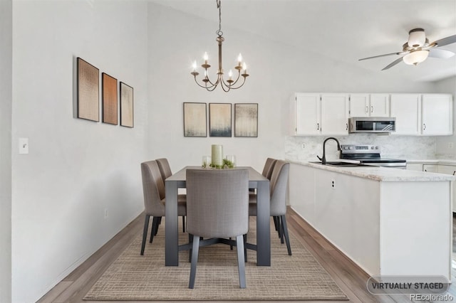 dining space with light wood-style flooring, ceiling fan with notable chandelier, and vaulted ceiling