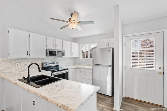 kitchen featuring a sink, a peninsula, white cabinets, a ceiling fan, and appliances with stainless steel finishes