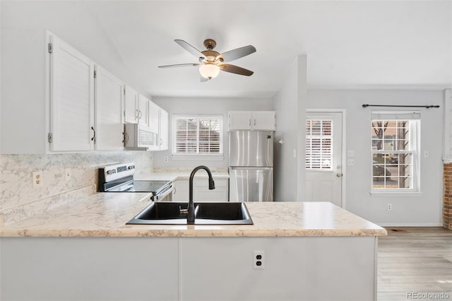 kitchen featuring ceiling fan, appliances with stainless steel finishes, light wood-type flooring, a sink, and a peninsula