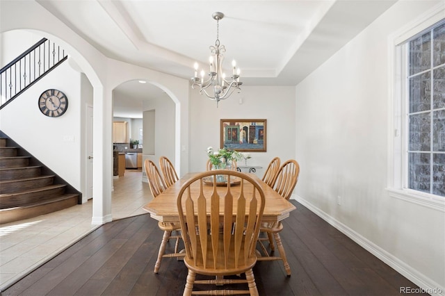 dining area with hardwood / wood-style floors, an inviting chandelier, and a tray ceiling