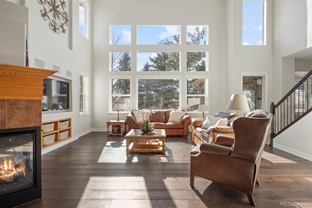 living room featuring dark hardwood / wood-style flooring, a tile fireplace, a healthy amount of sunlight, and a high ceiling