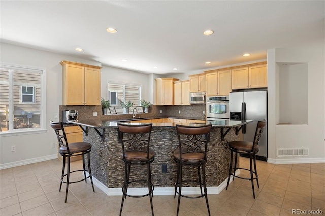 kitchen with light tile patterned floors, light brown cabinets, stainless steel appliances, and a kitchen bar