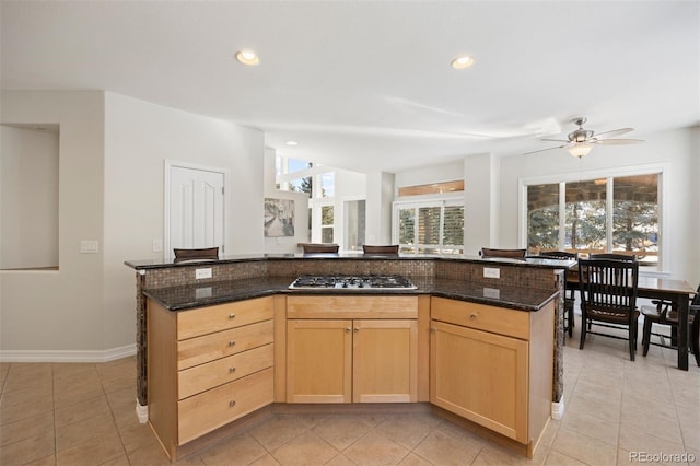 kitchen featuring stainless steel gas stovetop, light brown cabinetry, and dark stone counters