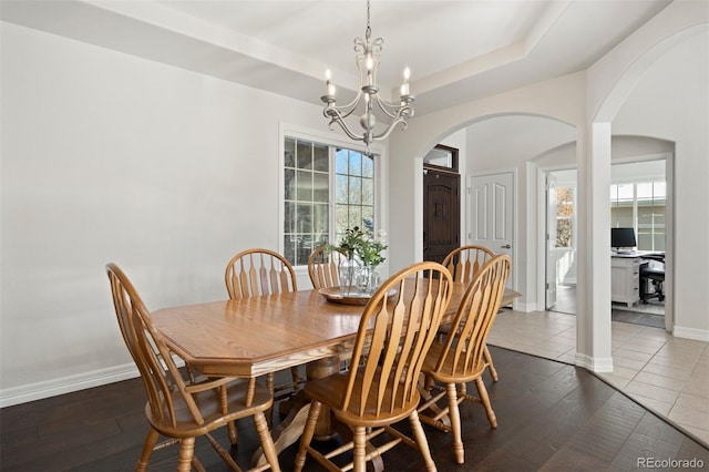 dining area with a tray ceiling, a chandelier, dark hardwood / wood-style floors, and a healthy amount of sunlight