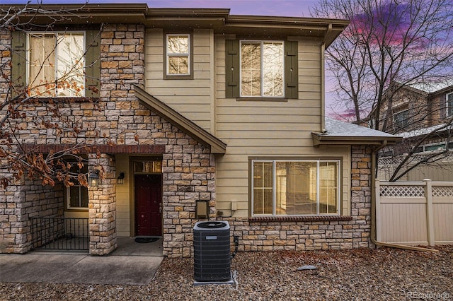 view of front of property with cooling unit, fence, and stone siding