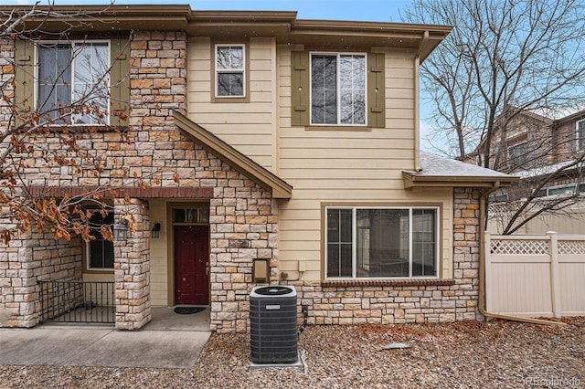 view of front of home featuring stone siding, central AC, and fence