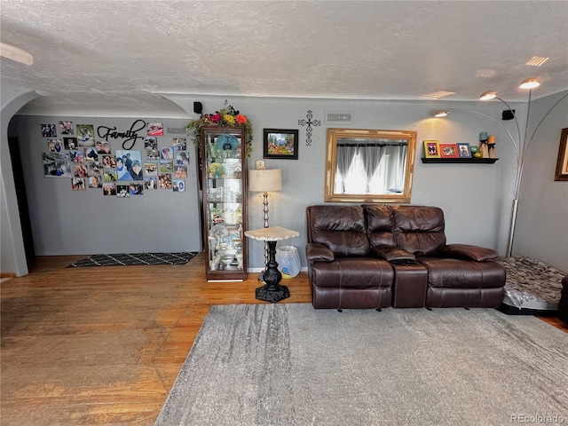 living room with a textured ceiling, arched walkways, wood finished floors, and visible vents