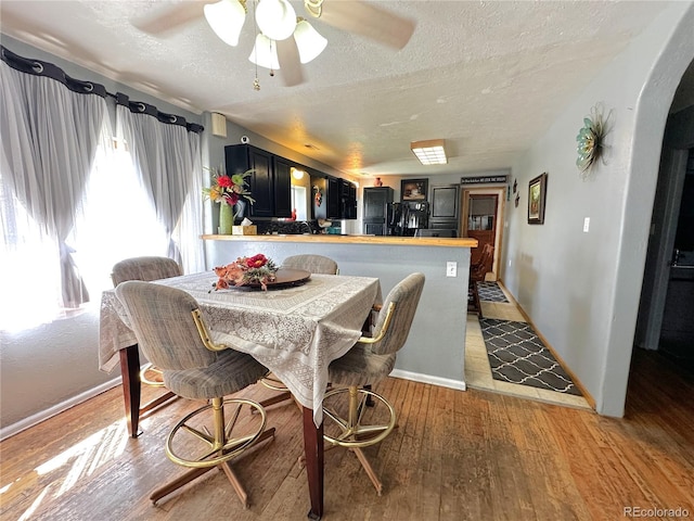 dining space with light wood-style floors, arched walkways, a textured ceiling, a ceiling fan, and baseboards