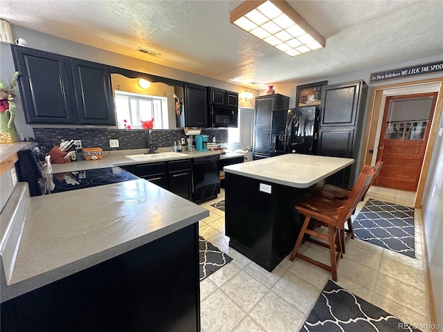 kitchen featuring a sink, light countertops, a breakfast bar area, decorative backsplash, and black appliances