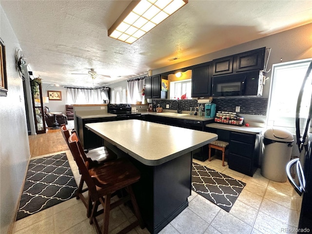 kitchen featuring black microwave, a sink, light countertops, a textured ceiling, and a peninsula