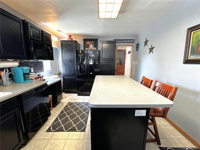 kitchen featuring a breakfast bar area, a kitchen island, light countertops, black appliances, and dark cabinetry