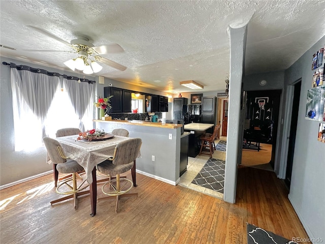 dining space with a ceiling fan, a textured ceiling, visible vents, light wood-type flooring, and baseboards