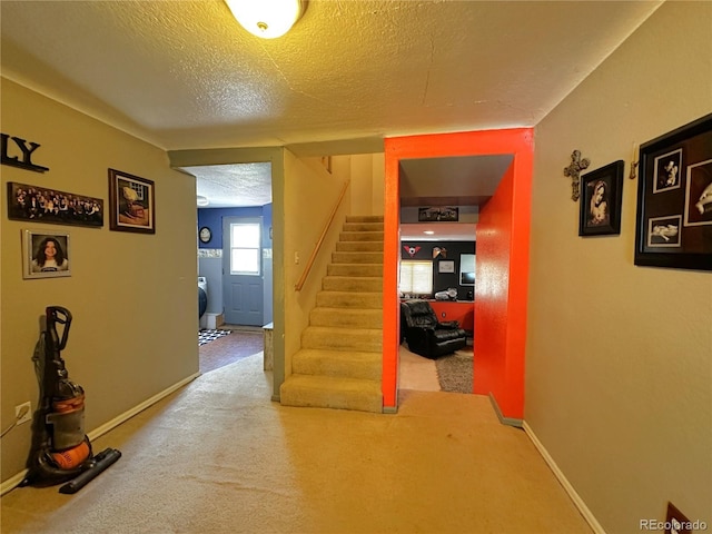 hallway featuring baseboards, carpet flooring, stairs, and a textured ceiling