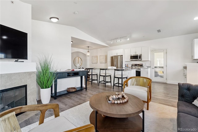 living room featuring lofted ceiling, rail lighting, a tile fireplace, and light hardwood / wood-style flooring